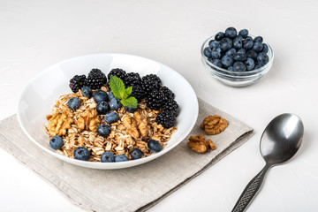 Healthy breakfast. Homemade granola, muesli, cereals with blackberries, blueberries, nuts, honey and mint in a white bowl on a white background.