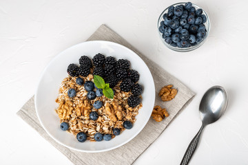 Healthy breakfast. Homemade granola, muesli, cereals with blackberries, blueberries, nuts, honey and mint in a white bowl on a white background.