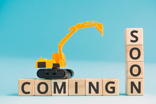 coming soon wooden cubes letters yellow toy excavator, development page under construction or technical work concept blue background