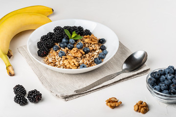 Healthy breakfast. Homemade granola, muesli, cereals with blackberries, blueberries, nuts, honey and mint in a white bowl on a white background.
