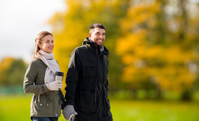 love, relationship and season concept - smiling couple with tumbler walking over autumn park background