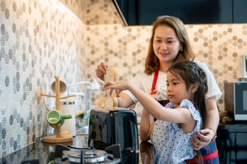 happy Mother teaching daughter making breakfast toast bread with toaster at home kitchen together ....