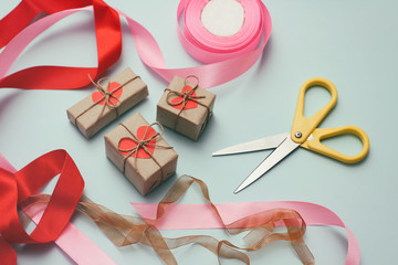 Gifts wrapping process. Decorative paper, silk ribbons, gift boxes, scissors. Light blue background. 