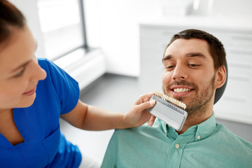 medicine, dentistry and healthcare concept - female dentist with tooth color samples choosing shade...