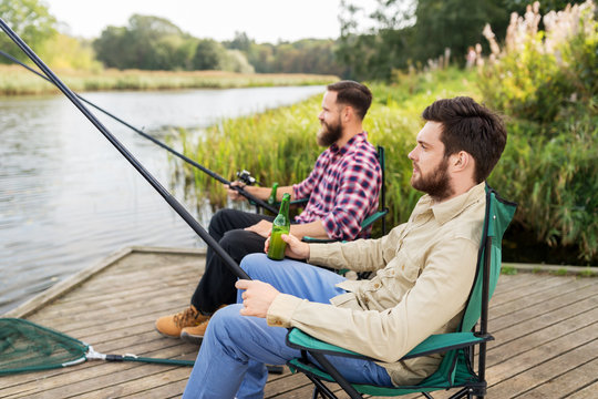 leisure and people concept - male friends fishing and drinking beer on lake