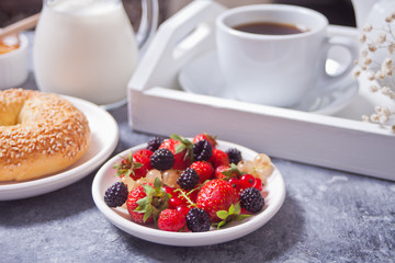 Fresh sweet berries on the white plate, bagel, cup of coffee and honey for breakfast.