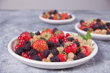 Healthy mixed berry with strawberry, blackberry, red and white currant on the different plates on concrete background. Top view. Copy space.