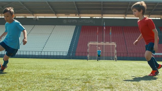 Small boy dribbling ball and avoiding opposite players in soccer match on grass stadium