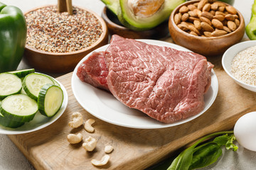raw meat on wooden chopping board near nuts and green vegetables, ketogenic diet menu