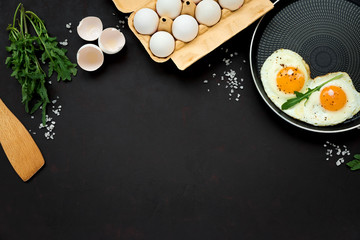 Fried eggs in frying pan with arugula leaves, salt and pepper for breakfast on black wooden background. Top view. Flat lay. Copy space. Healthy food concept