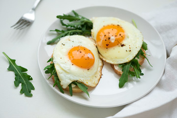 Sandwiches with ricotta cheese, arugula and fried egg on white wooden background. Selective focus. Healthy food concept