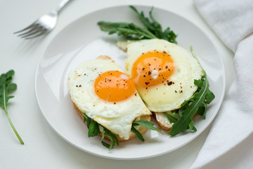 Sandwiches with ricotta cheese, arugula and fried egg on white wooden background. Selective focus. Healthy food concept