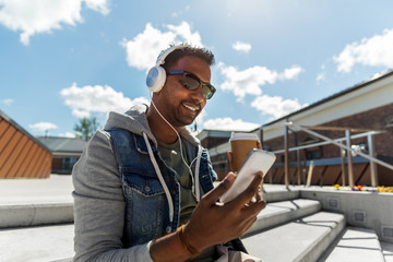 Fototapeta premium technology, leisure and people concept - indian man with headphones listening to music on smartphone on roof top
