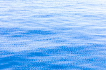 The background or texture of the blue water surface of the river, lake or sea with the waves, ripples and flares