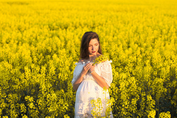 Naklejka na ściany i meble Pregnant girl with flowers in her hands. Belly of a pregnant woman. The concept of pregnancy. Blurred background over green nature. Pregnant tummy close up. spring park holding a bouquet.