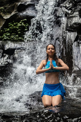 Young Caucasian woman meditating, practicing yoga at waterfall in Ubud, Bali, Indonesia. Close up.