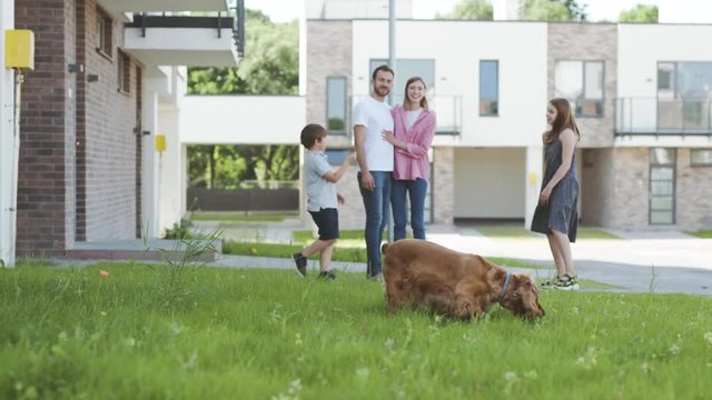 Amazing young family spending time outside walking with kids and a dog on a sunny summer day. Smiling excited siblings playing with a ball with puppy on the grass.
