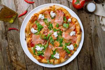 Pizza with salmon and Philadelphia cheese and aragula on wooden table