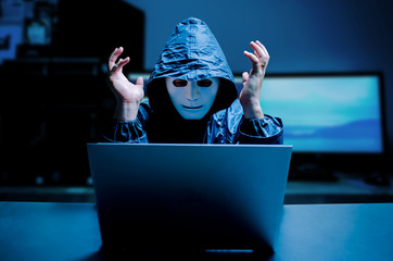 Anonymous computer hacker in white mask and hoodie. Stressful male hacker screaming on a damaged...