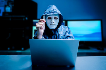 Anonymous computer hacker in white mask and hoodie. Obscured dark face holds a USB flash drive in his hands, Data thief, internet attack, darknet and cyber security concept, with copy space - obrazy, fototapety, plakaty