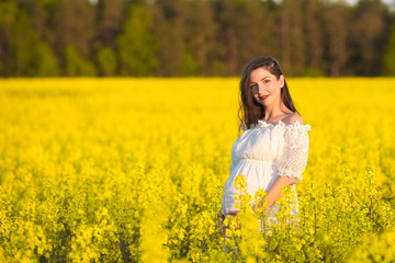 Fototapeta premium pregnant girl in a white dress. Outdoor natural portrait of beautiful pregnant woman in white dress