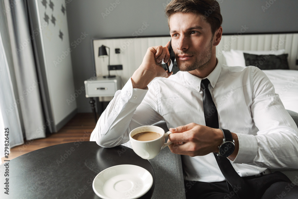 Sticker image of masculine young man talking on smartphone and drinking coffee in hotel apartment during bus