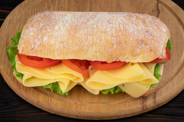 Ciabatta sandwich with lettuce , prosciutto and  cheese on wooden board