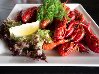 Red boiled crabs decorated with a salad, lemon and dill on a white plate on a black table. girl's hand takes one.