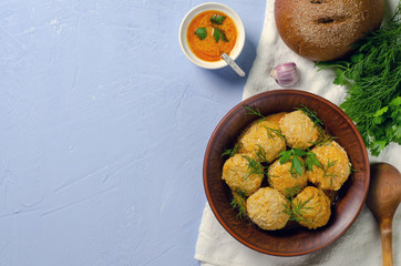 Delicious dinner: meatballs from minced meat with greens sauce and fragrant bread in a clay plate and with a wooden spoon on a blue background for the menu