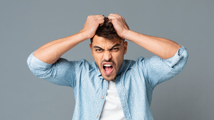 Frustrated Guy Pulling His Hair Out On Gray Studio Background
