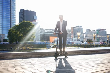 Obraz premium Young business man in a suit riding an electric scooter on a business meeting.
