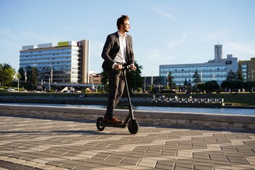 Young business man in a suit riding an electric scooter on a business meeting. © opolja