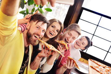 Selfie time concept. Friends eat pizza in a cafe, smile and shoot themselves on the camera smartphone