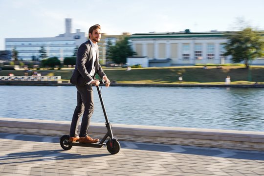 Young business man in a suit riding an electric scooter on a business meeting.