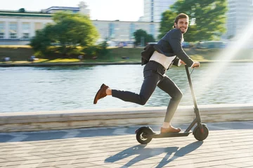 Foto op Plexiglas Young business man in a suit riding an electric scooter on a business meeting. © opolja
