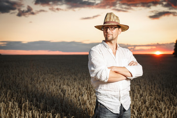 Farmer in a straw hat and glasses standing in a ripe wheat field before sunset.