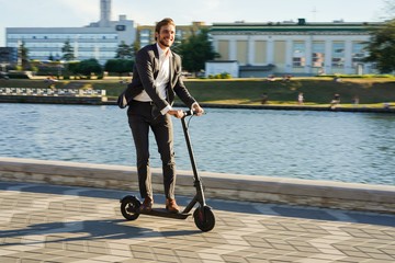 Young business man in a suit riding an electric scooter on a business meeting.