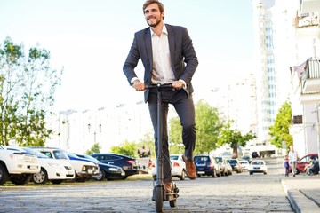 Young business man in a suit riding an electric scooter on a business meeting.