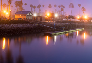 Foggy morning dims the reflecting lights on the smooth surface of the ocean cove dock water.