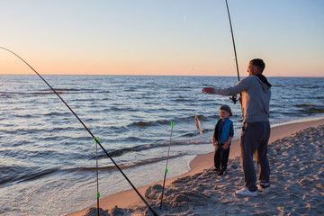 Father and son fishing on the beach of   Baltic Sea in the sunset time. 