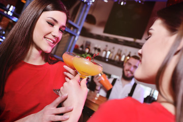two young cute girls drink cocktails in a nightclub or bar, have fun, smile and talk to the bartender