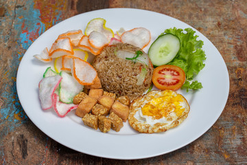 Fried rice with vegetables, rice chips, cheese tofu and fried egg on the old wooden table in local cafe, close up indonesian cuisine. Breakfast in Bali, Indonesia