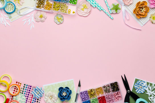 Paper flowers, tools, paper and scrapbooking items on pink background. Scrapbooking, top view, empty space for text in the center