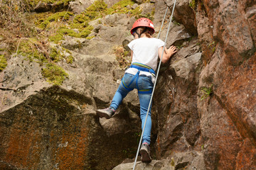 Fototapeta premium Little girl with protective equipment climbs up rock or mountain