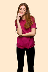 Young redhead girl looking down with the hand on the chin on isolated yellow background