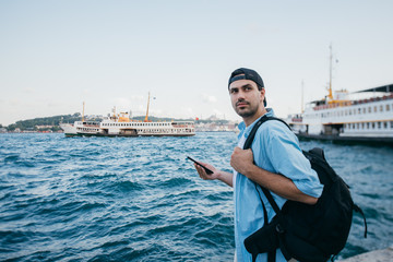 Portrait of a young man against the background of the sea, city, pier and ships.