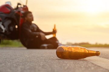 Motorcyclist sitting on the road beside his motorcycle and drinking an alcohol or beer
