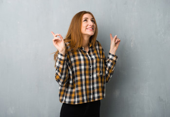 Young redhead girl over grunge wall pointing with the index finger a great idea