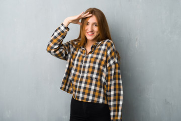 Young redhead girl over grunge wall saluting with hand