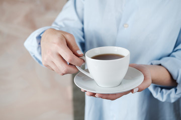 Woman holding cup of coffee. Female hands with cup of black tea on beige background. Close up